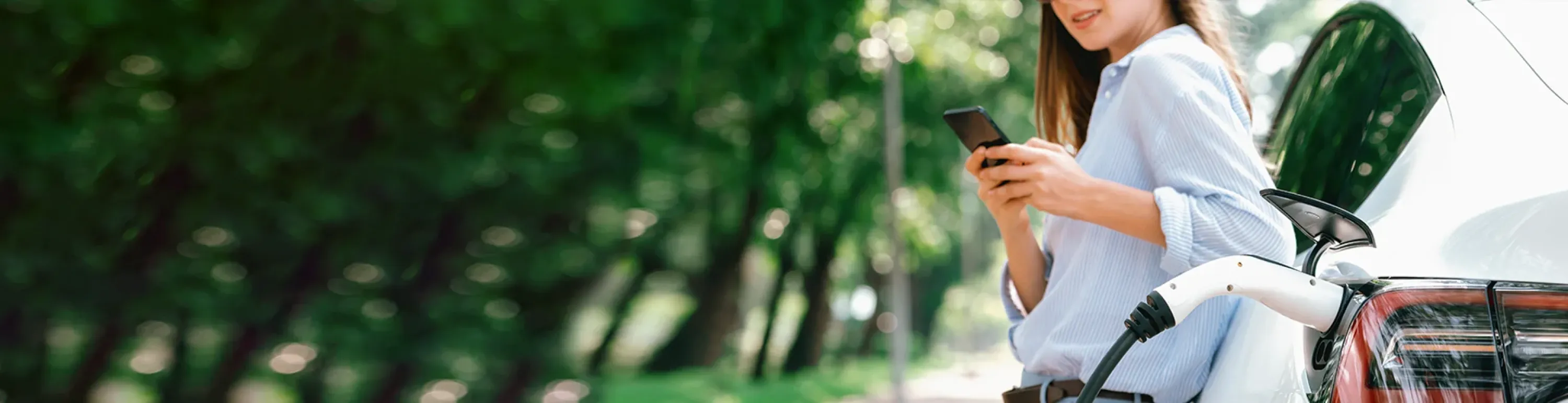 L&auml;chelnde Frau lehnt an Elektroauto und informiert sich &uuml;ber Elektromobilit&auml;t und das gesamte E-Wissen